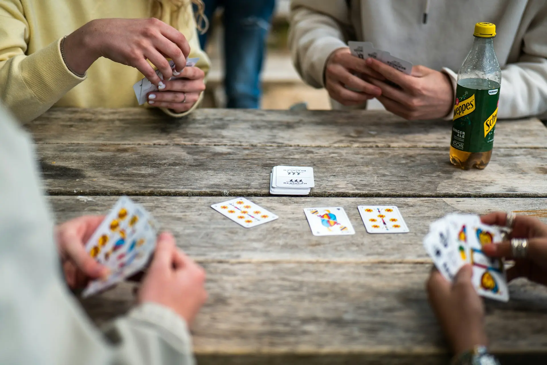 People play cards around a wooden table.